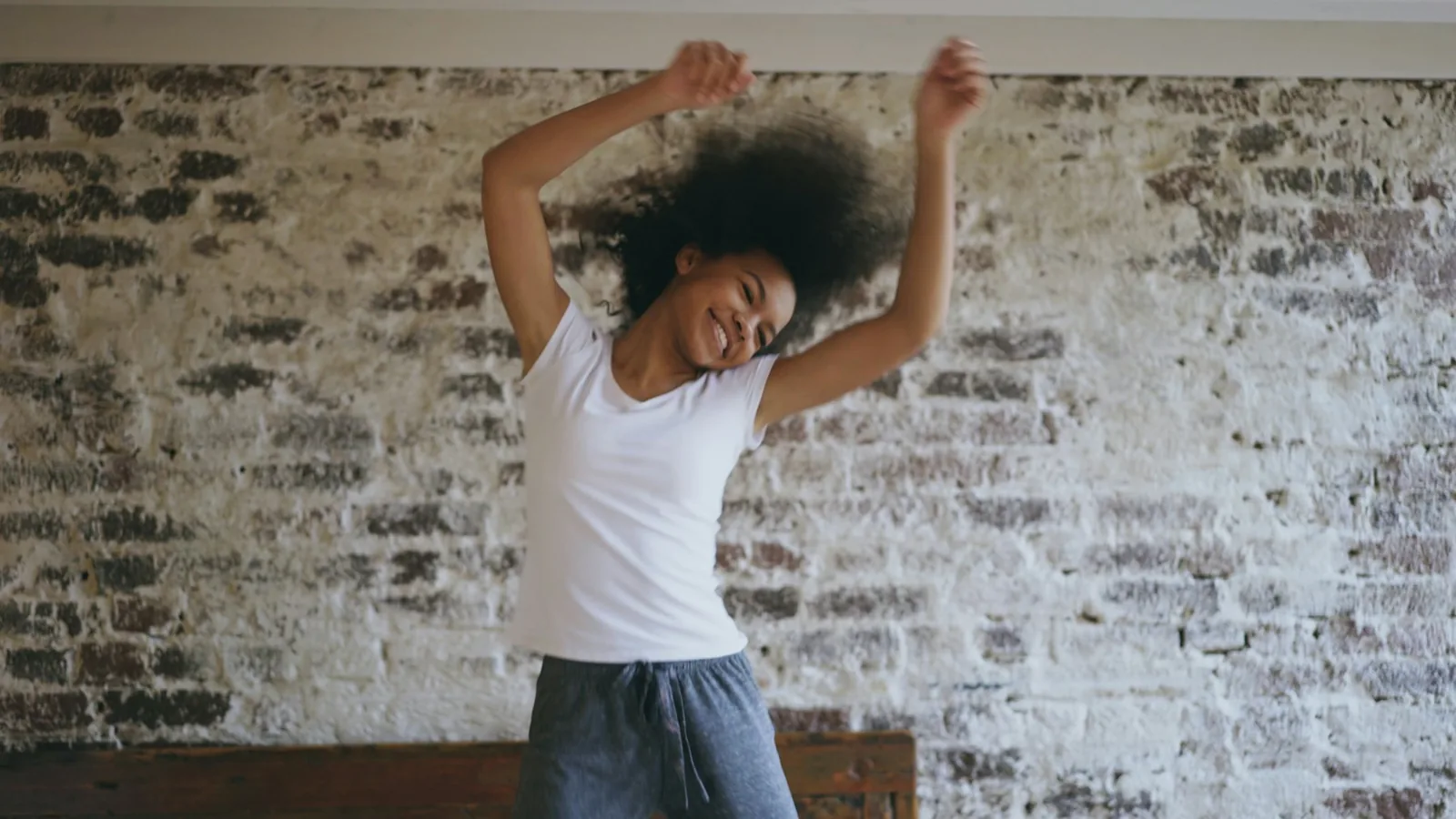 A woman smiling as she dances with her arms raised